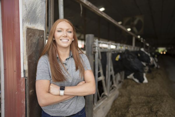 Picture of Megan Clancy, Farm Funders Risk Advisor standing in a dairy barn with black and white cows in the background